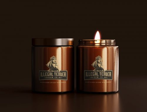 Front view of two Illegal Tender Rum Co limited-edition Bushtucker spiced candles. The right candle is lit, while the left candle is closed with the lid. Ideal liquor-inspired home decor.
